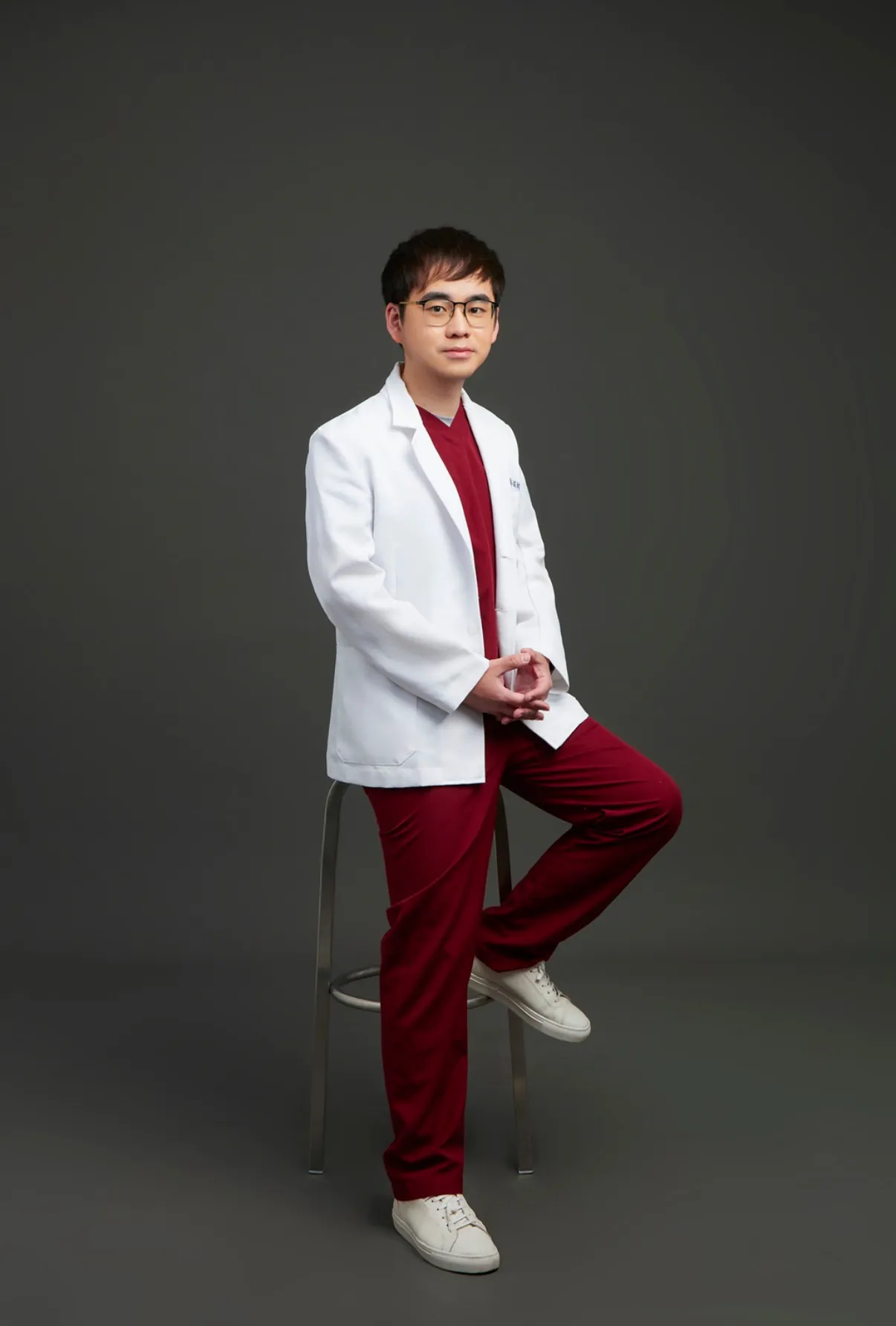 鄭穎翔獸醫師形象照，穿著酒紅色手術服與白袍